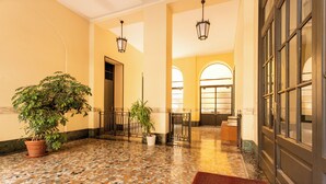 Um hall com piso de azulejos, plantas em vasos, tapete vermelho e uma grande janela com vista.
