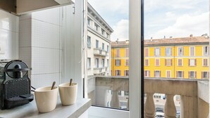 Cozinha com cafeteira, duas x ícaras e vista para prédios coloridos pela janela.
