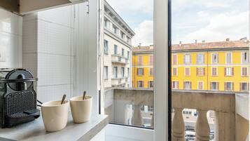 Una cucina con una macchina per il caffè, due tazze e vista su edifici colorati attraverso una finestra.