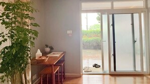 Huoneessa on puulattia, työpöytä tuolilla, ruukussa oleva kasvi ja liukuovi, joka johtaa ulos.