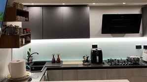 A modern kitchen with dark cabinets, a built-in oven, a coffee maker, and a flat-screen TV mounted above the counter. - Cozy and modern apartment (Pagliadiccio)