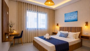 A hotel room with a bed, bedside tables, a desk, a chair, a large window with curtains, a hanging light fixture, and a painting on the wall. - Chic Boho Paradise w/ Parking, Rooftop & Workspace (Imi Ouaddar)