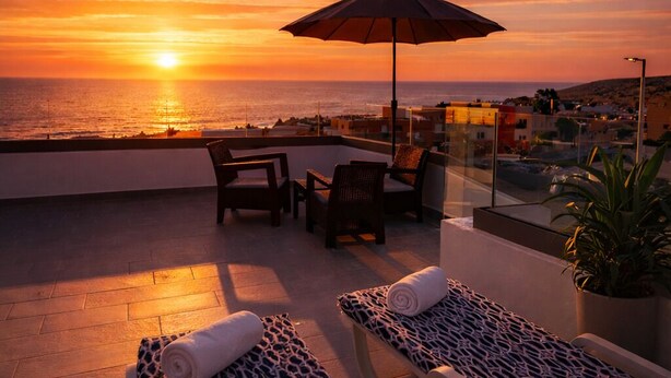 A rooftop terrace with lounge chairs, a table, and an umbrella, overlooking a sunset view. - Chic Boho Paradise w/ Parking, Rooftop & Workspace (Imi Ouaddar)