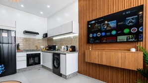 A modern kitchen with a built-in TV displaying various streaming services, a washing machine, and a compact dining area. - Chic Boho Paradise w/ Parking, Rooftop & Workspace (Imi Ouaddar)