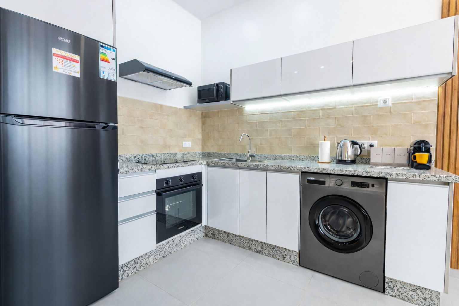 Eine moderne Küche mit einem Edelstahlkühlschrank, Backofen, Mikrowelle, Geschirrspüler und Waschmaschine.
