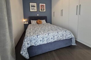 Ein Schlafzimmer mit einem Bett, einem Nachttisch, einer Lampe, einem Kleiderschrank und zwei gerahmten Bildern an der Wand.
