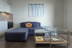 A modern, compact living space with a sofa, ottoman, and a glass coffee table with books.
