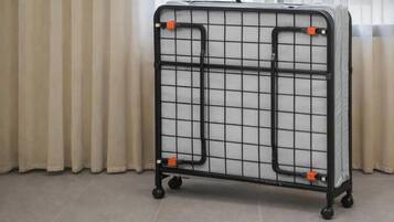 A metal storage cart with a grid pattern and wheels, positioned in a room with a curtain.