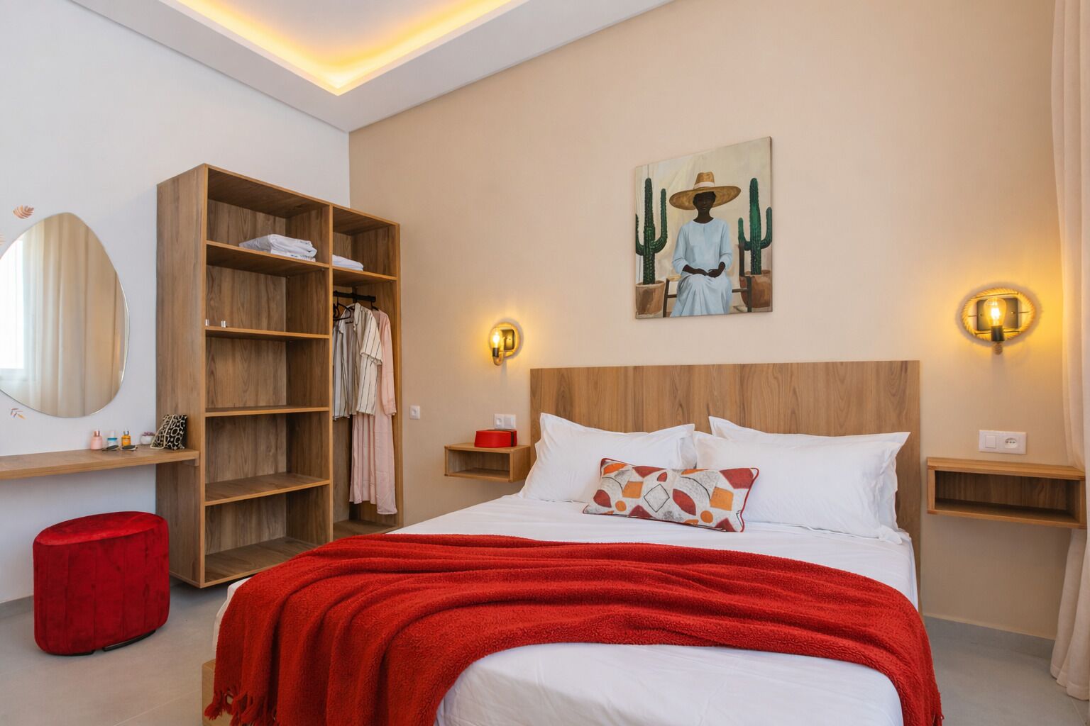 Ein Hotelzimmer mit einem Bett, einem Holzschrank, einem roten Hocker, einem Wandbild und zwei Nachttischen mit Wandleuchten.