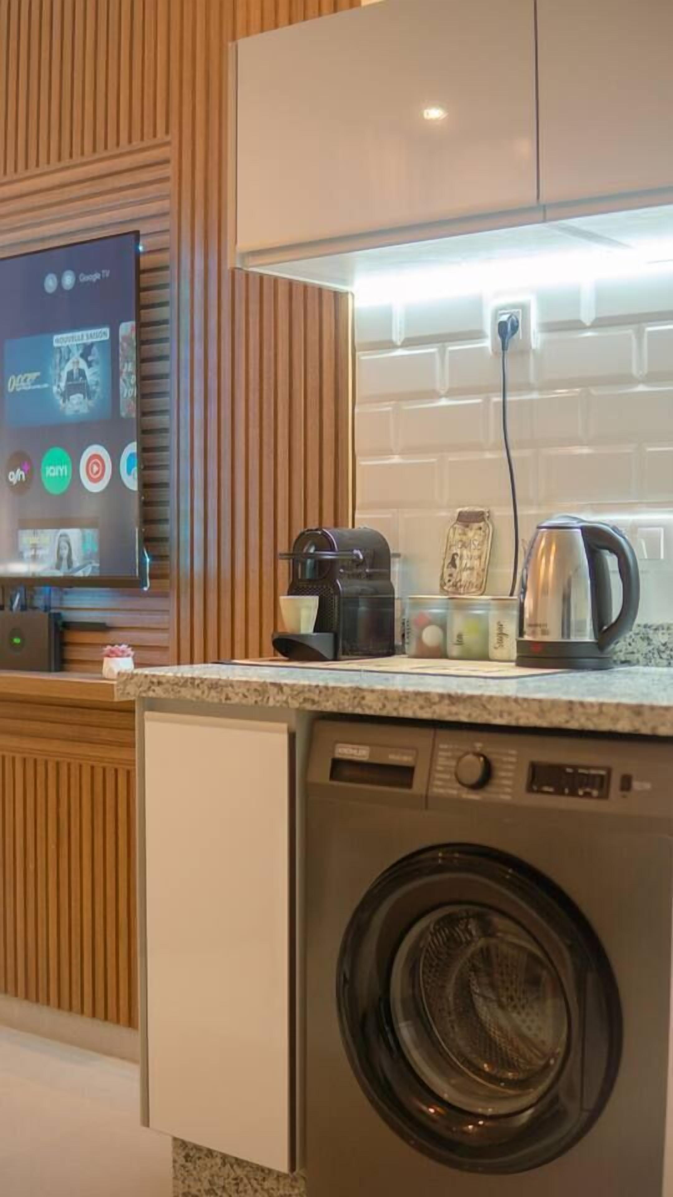 Ett kompakt kök med tvättmaskin, kaffebryggare och vattenkokare på bänkskivan.