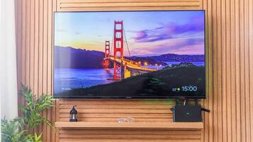 Een flatscreen-tv bevestigd aan een houten wand, met een landschapsafbeelding van een brug, een kleine plant en een decoratief object eronder.