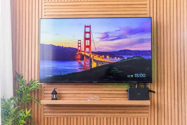 Un téléviseur à écran plat fixé sur un mur en bois, avec une image pittoresque d’un pont, une petite plante et un objet décoratif placé en dessous.