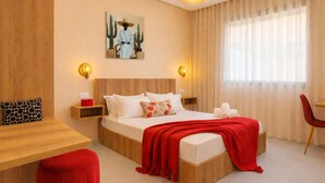 A modern hotel room with a wooden headboard, a large bed with white bedding and red accents, a red ottoman, a desk with a chair, and a painting on the wall. - Couple Haven•Workspace & WiFi 200Mb/s•Free Parking (Imi Ouaddar)
