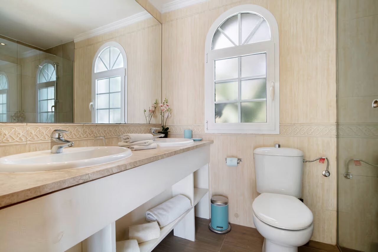 Une salle de bain avec deux lavabos, des toilettes, un miroir et une fenêtre.