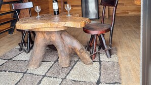 A rustic kitchen with a wooden table, chairs, a refrigerator, and a wine rack.