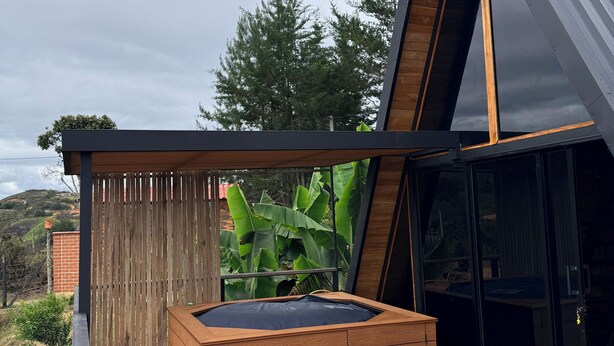A modern outdoor deck with a hot tub, wooden furniture, and a metal roof.