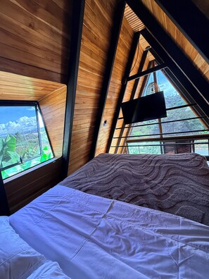 A bedroom with a bed, a TV, and a window with a view of greenery. - Cabin with a private hot tub and a view of the mountains (Guarne)