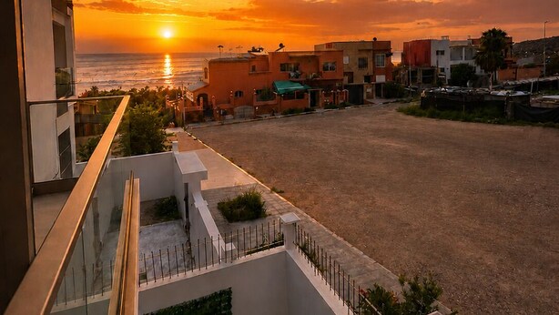 A balcony with a view of the sunset over the sea, a sandy area, and a row of buildings. - Luxury Berber Chic•3mn to Beach•Rooftop•Balcony•AC (Imi Ouaddar)