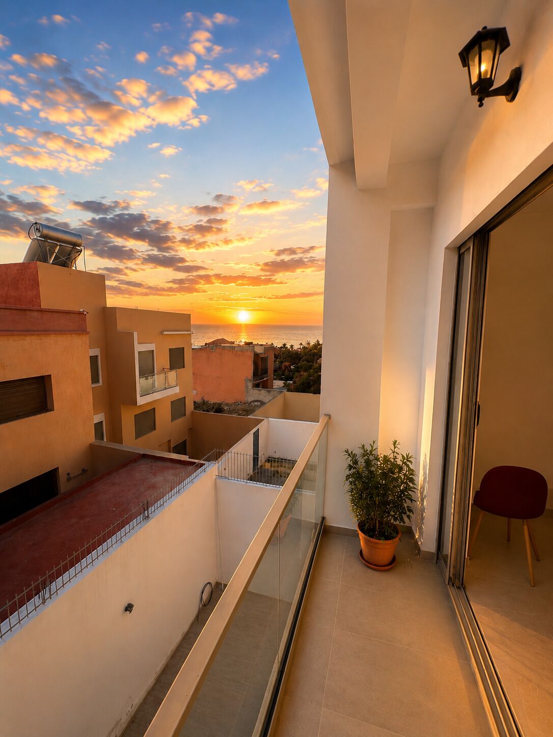A balcony with a view of the sunset, a potted plant, and a red chair.