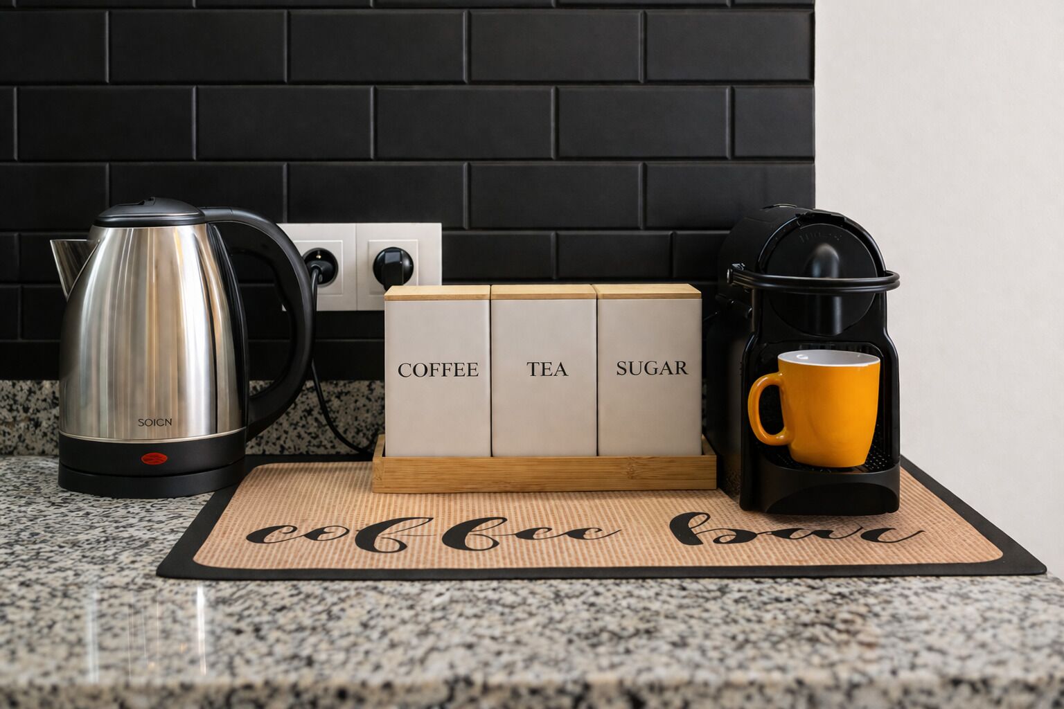 A kitchen counter with a coffee maker, a kettle, and a sugar and tea dispenser.