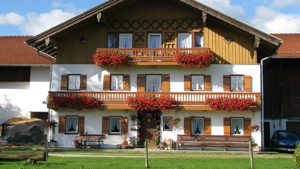 A traditional chalet with a wooden balcony, multiple windows, and a bench outside. - "Zuhaus" Vacation Rental on the 1st Floor, 70 square meters (Siegsdorf)