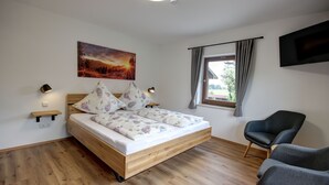 A bedroom with a wooden bed, a mounted TV, a window with curtains, and a chair. - "Zuhaus" Vacation Rental on the 1st Floor, 70 square meters (Siegsdorf)