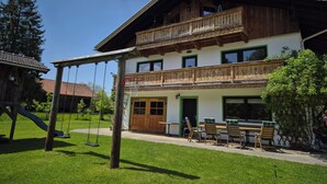 A two-story building with a balcony, a swing set, and outdoor seating. - "Zuhaus" Vacation Rental on the 1st Floor, 70 square meters (Siegsdorf)