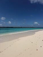Uma praia com águas turquesa cristalinas, areia branca e uma faixa de terra ao longe.