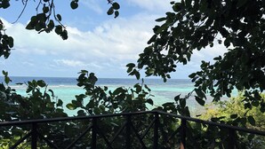 A wooden deck with a railing, overlooking a beach with clear turquoise water and a partly cloudy sky.