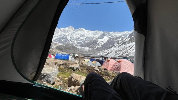 Una carpa con vistas a montañas nevadas y otras carpas al fondo.