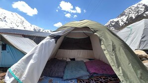 Una carpa con zona de dormir en su interior, rodeada de otras tiendas y un paisaje montañoso.