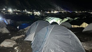 Vista nocturna de tiendas de campaña instaladas sobre un terreno rocoso, con montañas al fondo.