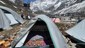 Un camping con tiendas de campaña, terreno rocoso y montañas al fondo.
