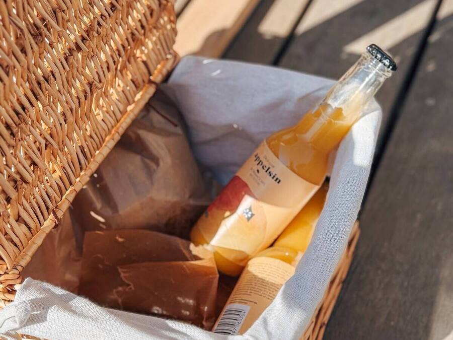 Una cesta de mimbre con una botella de vino y dos barras de chocolate.