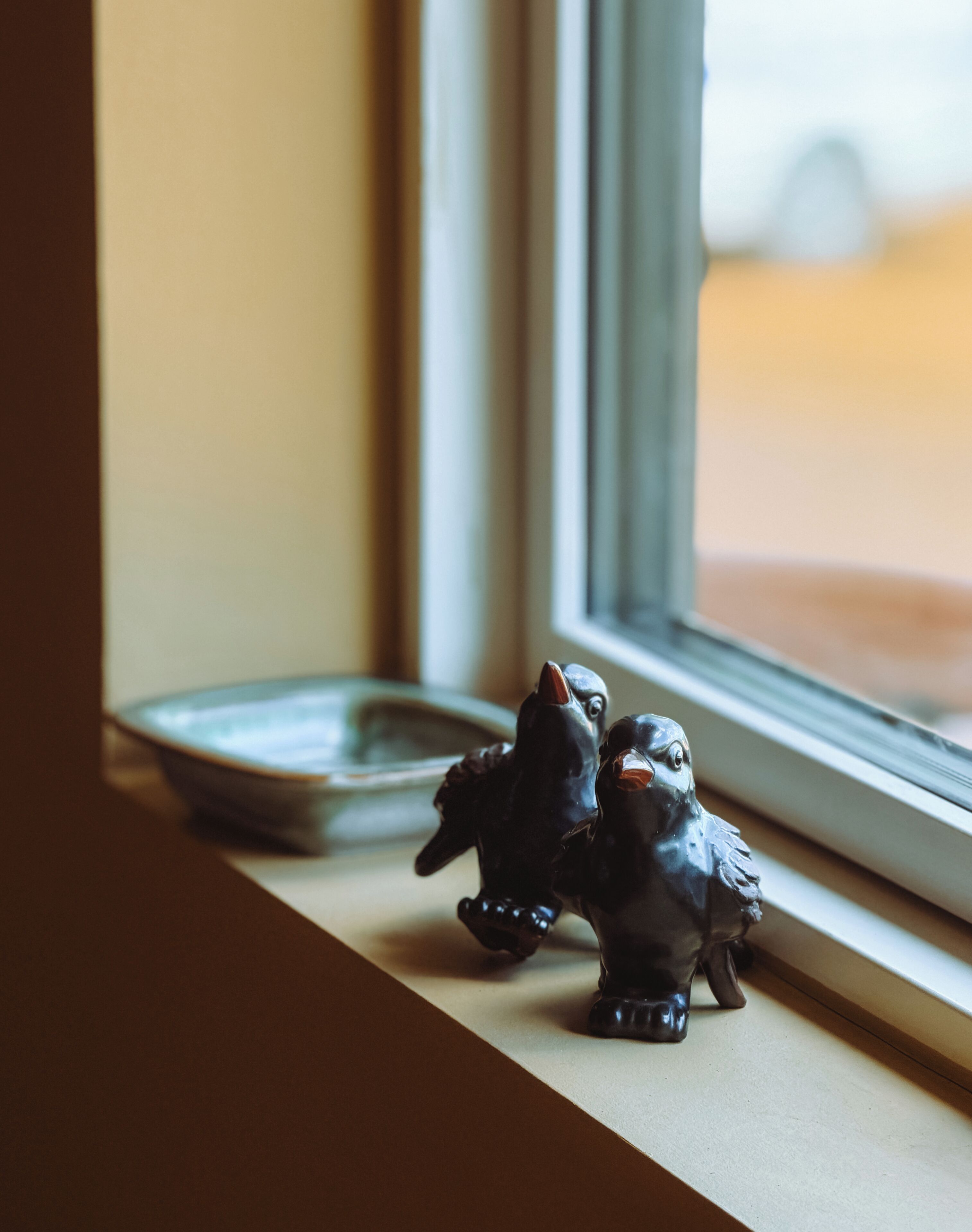 A window sill with two bird figurines and a small dish.