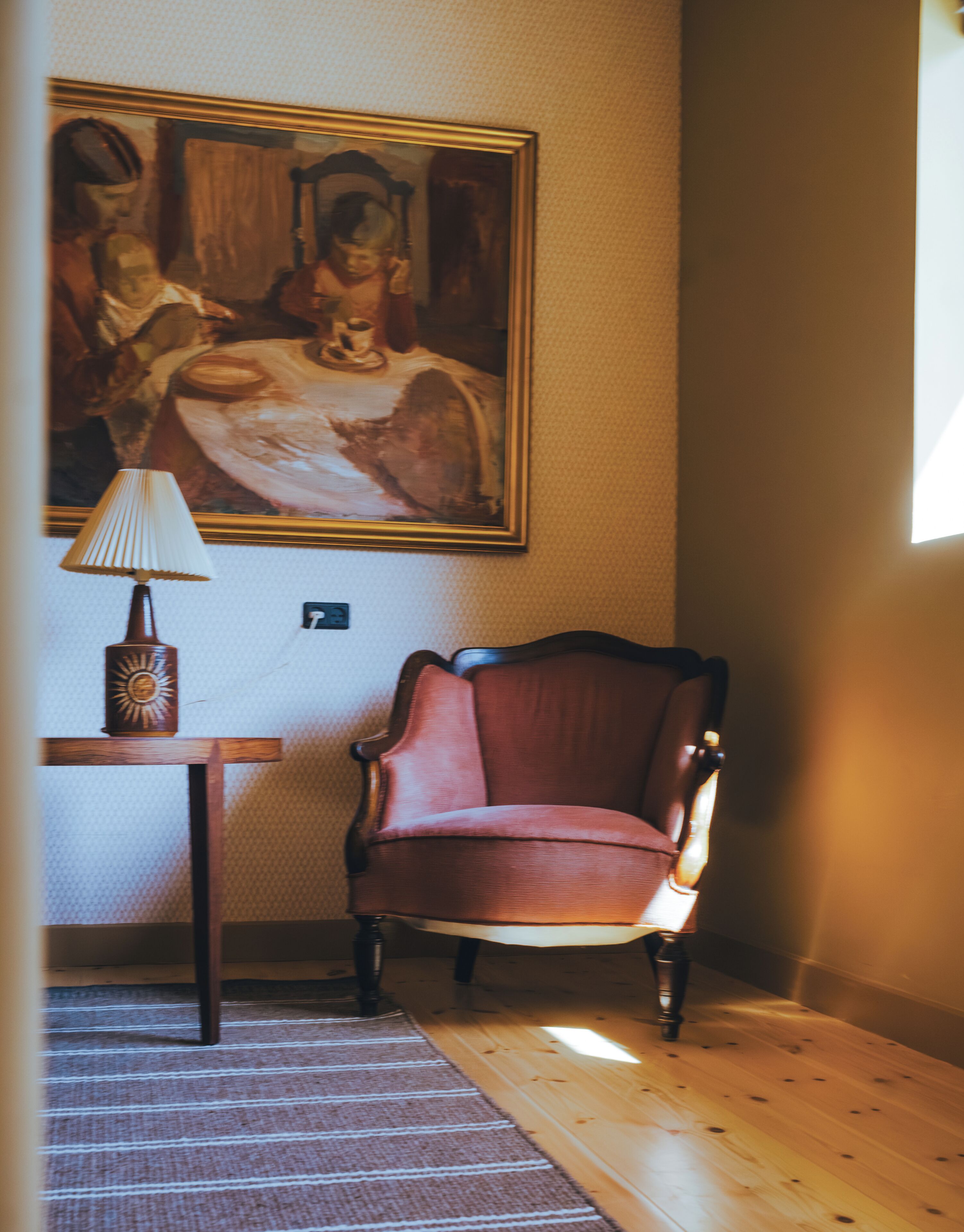 Une pièce avec un plancher en bois, un fauteuil rouge, une lampe et un tableau accroché au mur.