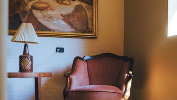 Une pièce avec un plancher en bois, un fauteuil rouge, une lampe et un tableau accroché au mur.