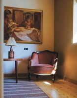 Une pièce avec un plancher en bois, un fauteuil rouge, une lampe et un tableau accroché au mur.