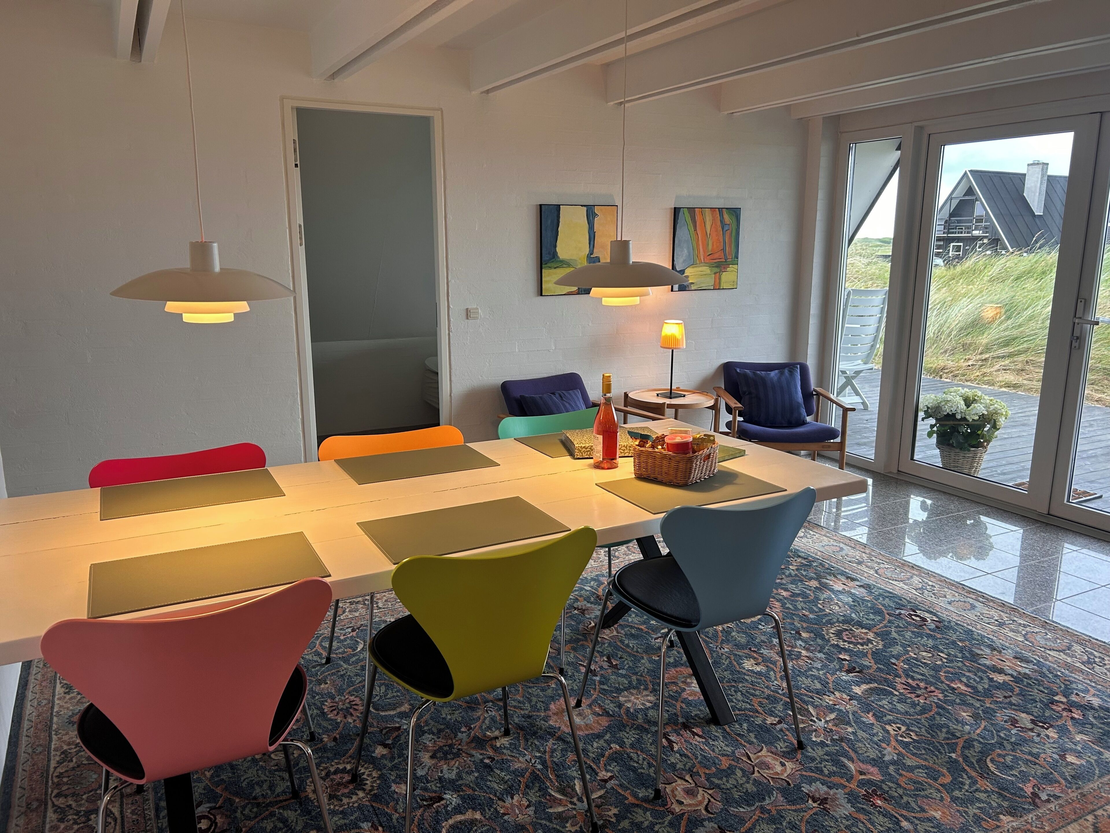 Un comedor con una mesa larga, sillas coloridas y vistas al exterior a través de amplios ventanales.