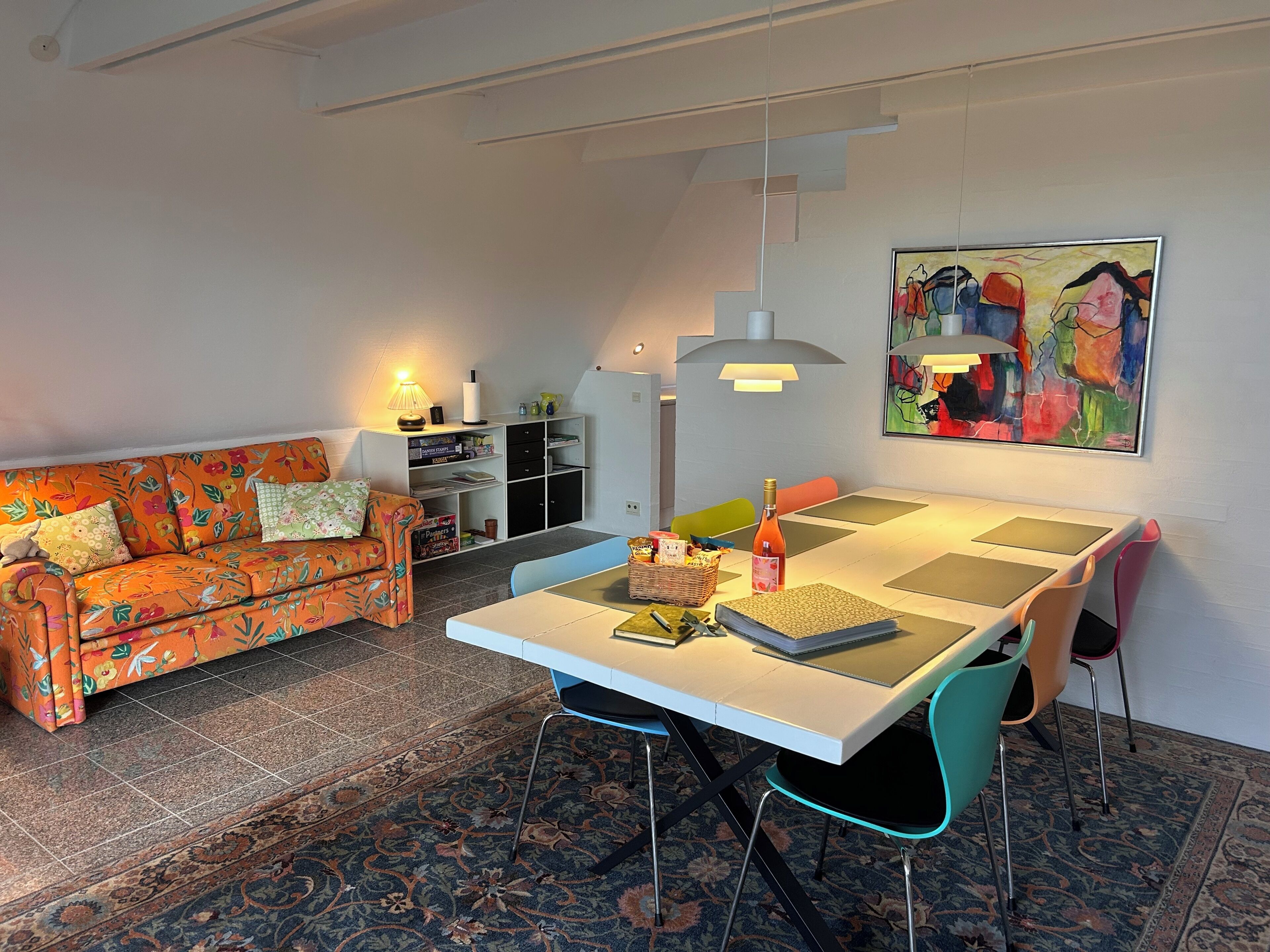 A modern living room with a sofa, dining table, chairs, a bookshelf, and a painting.