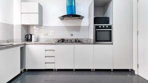 A modern kitchen with white cabinets, a blue range hood, a built-in oven, and a countertop with a kettle. - Cozy 3 Bedroom Apartmen -Swimming Pool & Gym QQ (Lagos)