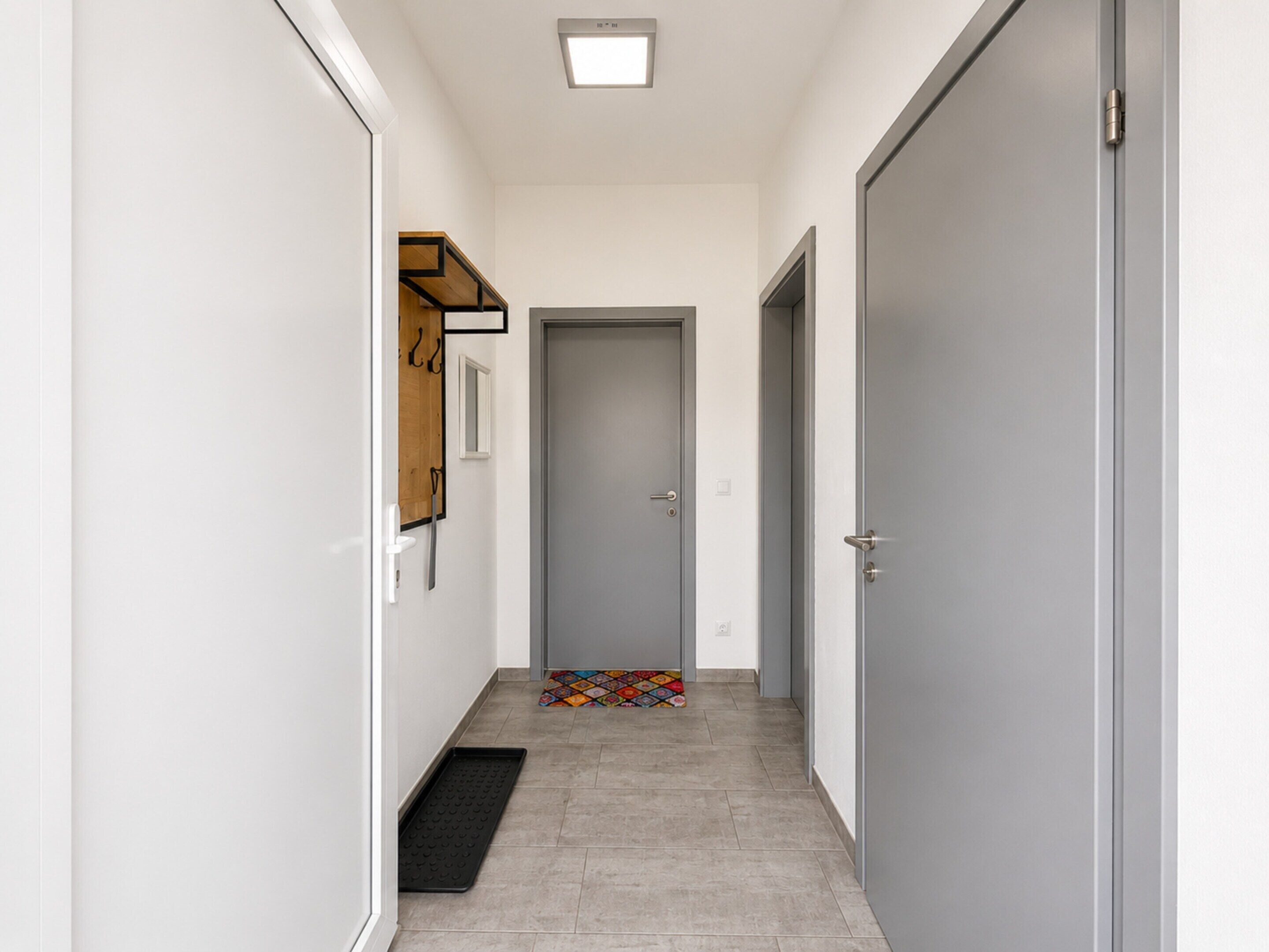 A narrow hallway with a door at the end, a small rug, and a wall-mounted coat rack.