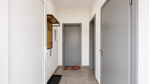 Een smalle gang met een deur aan het einde, een klein vloerkleed en een kapstok aan de muur.