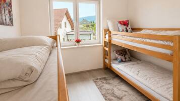 A bedroom with a bunk bed, a single bed, a window with a view of houses, and a painting on the wall.