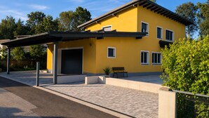 Een modern geel huis met een overdekte oprit en een bankje.
