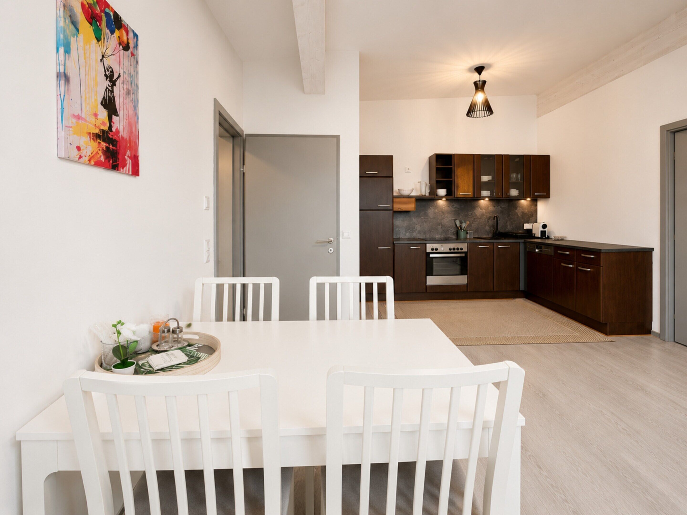 A modern kitchen with dark wooden cabinets, a stainless steel oven, and a dining area with white chairs and a table.