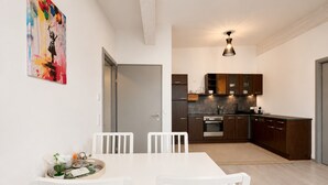 Een moderne keuken met donkere houten kastjes, een roestvrijstalen oven en een eethoek met witte stoelen en een tafel.