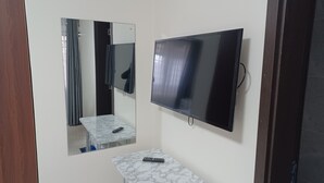 Ett rum med en platt-TV som är monterad på väggen, ett bord med marmorliknande mönster och en spegel som reflekterar en del av rummet.