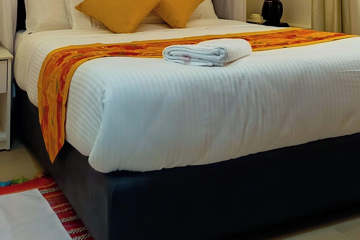 A hotel room with a bed, curtains, a nightstand, and a bedside table.