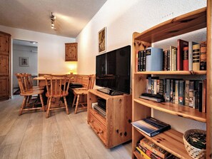 Ein gemütliches Wohnzimmer mit einem Holzboden-TV-Schrank, einer Bücherwand voller Bücher und einem Essbereich mit Holzsesseln und einem Tisch.